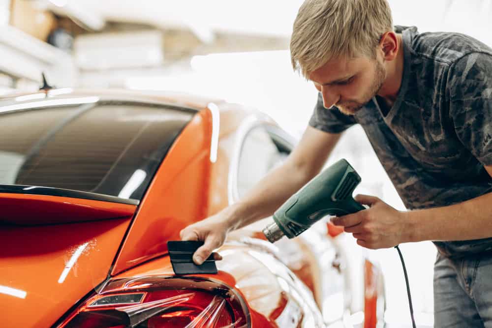 Man car wrapping with foil and drying with fan at a car service